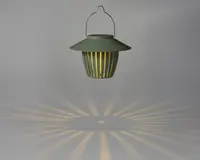 En hængende lanterne med mat grøn finish og en bred, skrånende top. Lanternen har lodrette lameller rundt om kroppen, som lader varmt lys skinne igennem og skaber et dekorativt stjernemønster på overfladen nedenunder. Den har et metalhåndtag til nem transport eller ophængning.