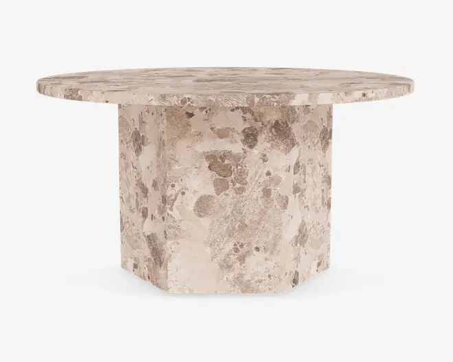 Rundt bord med en kraftig, solid stentop og en robust, geometrisk piedestalbase. Overfladen og basen har et naturligt, plettet beige og taupe stenmønster, der giver et tekstureret og jordnært udtryk. Bordpladens kanter er let affasede for et elegant finish.