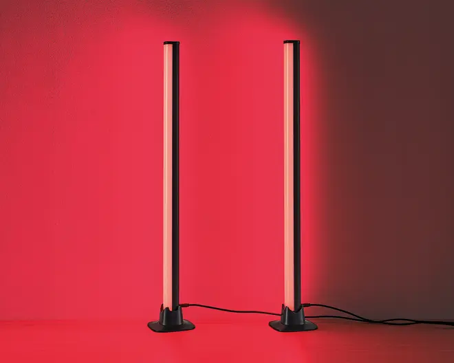 Et par slanke, lodrette LED-lysstænger med sorte baser, der udsender et kraftigt rødt skær. Lysene står side om side, hver med en strømledning, der går ud fra basen. Designet er minimalistisk og moderne, velegnet som accent- eller stemningsbelysning i nutidige indretninger.