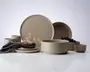 Et sæt matte beige stentøjstallerkener og skåle med et minimalistisk design. Sættet indeholder store og små tallerkener, dybe skåle og små kopper. Kanterne er glatte og let afrundede, hvilket giver et moderne og elegant udtryk. En mørkegrå stofserviet med en brun læderring og tørrede blomster ligger på en af tallerkenerne som dekoration. Det samlede udtryk er enkelt og moderne, velegnet til både hverdags- og festbrug.