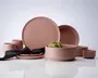 Et sæt mat, støvet rosa keramisk service bestående af tallerkener, skåle, kopper og små skåle. Delene har et glat, minimalistisk design med rene linjer og uden synlige mønstre eller dekorationer. Sættet indeholder en stor middagstallerken, en mindre tallerken, en dyb skål, en lav skål, to kopper og to små skåle. Overfladerne er ensartede i farve og tekstur, hvilket giver et moderne og elegant udtryk. En sort stofserviet er lagt over en af tallerkenerne, og en artiskok ligger i den dybe skål.