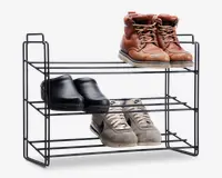 Trestykket metalreol med et minimalistisk, åbent design og vandrette stænger til opbevaring af sko. Reolen viser tre par sko: brune læderstøvler, sorte træsko og grå sportssko. Konstruktionen er let, har håndtag i siderne for nem transport, og hylderne har god afstand til forskellige skostørrelser.