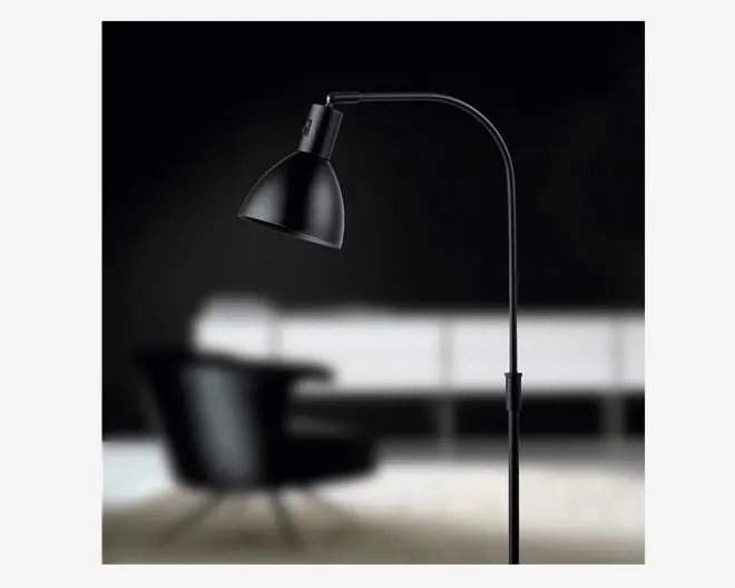 En elegant, moderne standerlampe med mat sort finish. Lampen har en buet arm, der strækker sig udad og holder en konisk lampeskærm med let udvidet kant. Lampens hoved kan justeres, så lyset kan rettes, og den har et slankt, minimalistisk stel og fod, hvilket gør den velegnet til moderne indretning.
