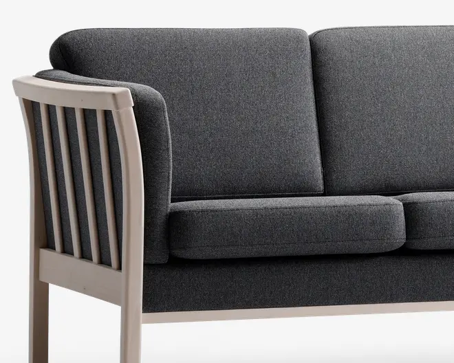 Nærbillede af en sofa med mørkegråt stofbetræk og tykke, rektangulære sæde- og ryghynder. Armlænet og rammen er lavet af lyst træ med lodrette lameller på siden, hvilket giver et moderne og robust udtryk.