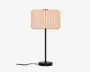 En bordlampe med en cylindrisk, plisseret skærm i lys beige, en slank sort stamme og en rund sort base, med ledningen synlig nederst.