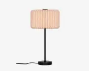 En bordlampe med en cylindrisk, plisseret skærm i lys beige, en slank sort stamme og en rund sort base, med ledningen synlig nederst.