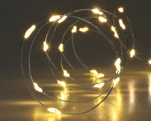 Et nærbillede af en fleksibel, tynd sølvtråd med små, jævnt fordelte LED-lys i varm hvid. Tråden er snoet i en løs spiral, og lysene udsender et blødt, varmt skær, der skaber en hyggelig og indbydende stemning. Overfladen nedenunder reflekterer lyset og forstærker den samlede lysstyrke og atmosfære.