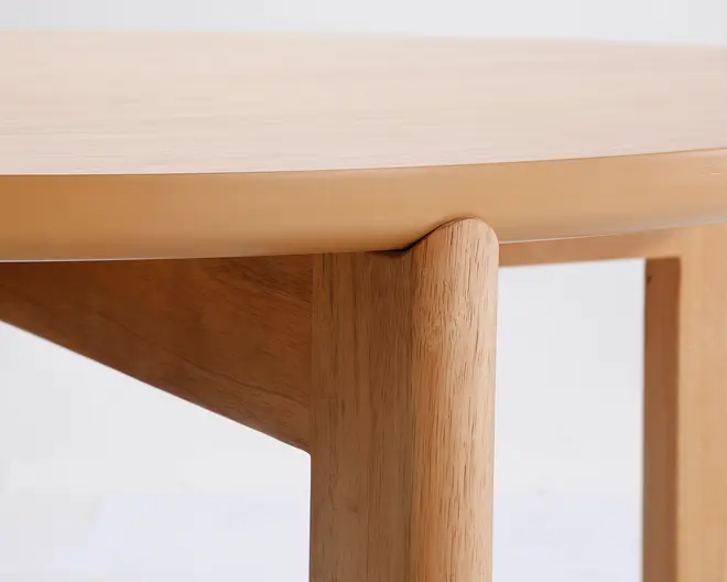Nærbillede af et hjørne på et bord i lyst træ, hvor den afrundede bordkant og det glatte samlingspunkt mellem bordben og bordplade fremhæves. Træets årer er synlige, og overfladen fremstår glat og mat, hvilket giver et naturligt og minimalistisk udtryk.