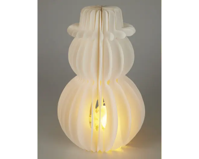 Lampe med en skulpturel, snemand-lignende form lavet af sammenlåsende hvide paneler. Panelerne er jævnt fordelt og skaber en rillet, åben struktur, der lader lyset skinne igennem. Pæren er synlig indeni og udsender et varmt, diffust skær. Designet er moderne og dekorativt, velegnet som et accentstykke i nutidige indretninger.