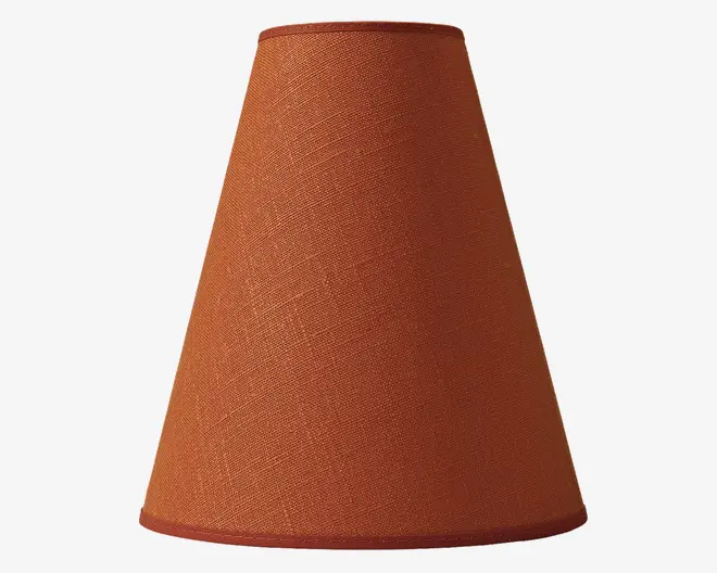 En konisk lampeskærm med en tekstureret stofoverflade i en varm terrakottafarve. Skærmen har et glat, ensartet udseende med matchende kantbånd øverst og nederst. Stoffet har et diskret vævet mønster, der giver et let rustikt og hyggeligt udtryk.