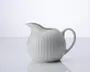 En lille, rund hvid keramikkande med rillet tekstur på overfladen. Den har en bred tud, der gør det nemt at hælde, og et buet håndtag for et behageligt greb. Designet er enkelt og elegant, velegnet til servering af fløde eller mælk.