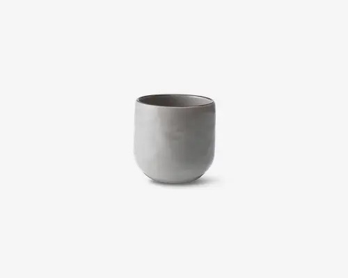 En minimalistisk, cylindrisk kop med en glat, mat hvid overflade. Koppen har en afrundet bund og lige sider uden hank eller synlige dekorationer. Det enkle design giver et moderne og elegant udtryk.