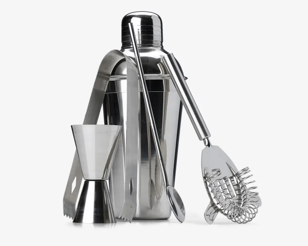 Et sæt barværktøj i rustfrit stål, der inkluderer en cocktailshaker med tætsluttende låg, en dobbeltsidet målebæger til væsker, en lang røreske, en fjeder cocktail-si og et par istænger. Alle dele har en blank, poleret overflade og er designet til holdbarhed og nem rengøring.
