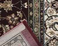 Nærbillede af et traditionelt mønstret tæppe med indviklede blomster- og vinmønstre i nuancer af bordeaux, creme, olivengrøn og beige. Tæppet har en detaljeret kant med gentagne blomstermotiver og en tæt vævet bagside for holdbarhed. Kanten er afsluttet med en bordeaux kant for at forhindre, at det frynser.