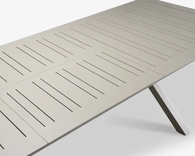 Rektangulært bord med lys beige finish, der har jævnt fordelte smalle lameller, som løber på langs af bordpladen. Bordet har et moderne, minimalistisk design med rene linjer og skråtstillede ben. Den lamelopdelte overflade giver et moderne udtryk og kan hjælpe med vandafledning, hvis bordet bruges udendørs.