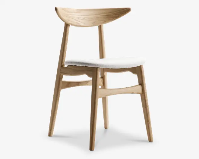 Stol med en ramme af lyst træ med naturlig finish, let tilspidsede ben og en bred, buet ryglæn for ergonomisk støtte. Sædet er polstret med et lysefarvet stof, hvilket giver komfort og et rent, moderne udtryk. Designet er minimalistisk og skandinavisk inspireret med fokus på enkelhed og funktionalitet.