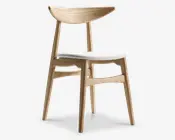 Stol med en ramme af lyst træ med naturlig finish, let tilspidsede ben og en bred, buet ryglæn for ergonomisk støtte. Sædet er polstret med et lysefarvet stof, hvilket giver komfort og et rent, moderne udtryk. Designet er minimalistisk og skandinavisk inspireret med fokus på enkelhed og funktionalitet.