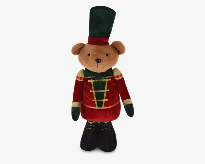 Bamse med blød, lysebrun pels iført en festlig soldateruniform. Uniformen består af en høj mørkegrøn hat med rød bånd, en rød velourjakke med guldfarvede detaljer og grønne accenter samt sorte støvler med guldsnørebånd. Bamsen har et venligt, broderet ansigt.