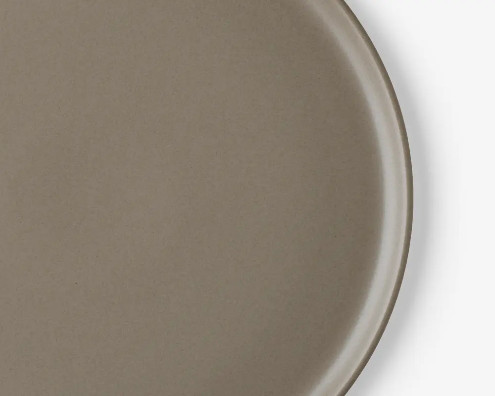 Et nærbillede af en rund tallerken med en glat, mat taupe-farvet overflade. Tallerkenen har en let forhøjet kant og et minimalistisk design uden mønstre eller dekorationer.