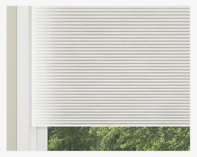 Hvid, vandret plisseret vinduesafdækning med et rent og moderne udseende. Materialet ser ud til at være lysfiltrerende, så noget naturligt lys slipper igennem, samtidig med at det giver privatliv. Plisseringerne er jævnt fordelt, og kanterne er pænt afsluttede. Gardinet er delvist trukket ned, så man kan se grønne træer udenfor.