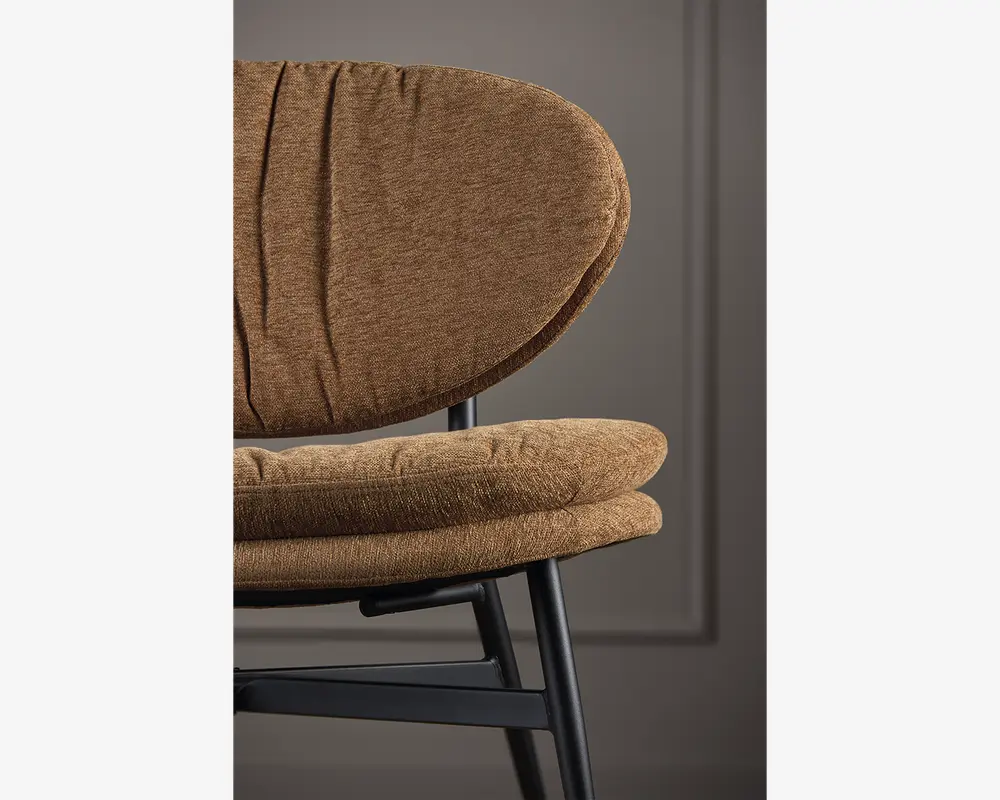 Nærbillede af en stol med en blød, rund ryg og en tyk, polstret sædehynde, begge betrukket med et tekstureret brunt stof. Stolen har en solid sort metalramme med et moderne, minimalistisk design. Stoffet ser blødt og behageligt ud, og lette folder giver et afslappet udtryk.