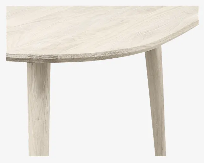 Nærbillede af et bord i lyst træ med en glat, afrundet kant og synligt træmønster. Bordet har solide, let tilspidsede ben, der matcher bordpladens finish.