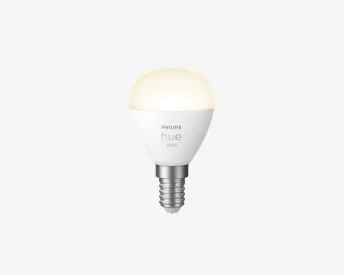 Kompakt LED-pære med mat hvid kuppel og metal skruefatning. Pæren har Philips Hue-logoet og er mærket 'white'. Den har en lille E14 sokkel, der passer til mindre lamper, og udsender et blødt hvidt lys. Designet er moderne og minimalistisk.