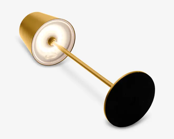 Elegant, moderne lampe med en cylindrisk lampeskærm i guldfarve og en matchende guldfarvet stang. Lampen har en rund sort fod for stabilitet og en hvid inderside, der hjælper med at sprede lyset jævnt. Det samlede design er minimalistisk og stilfuldt, velegnet til moderne indretning.