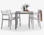 Et moderne udendørs spisesæt bestående af et rektangulært hvidt bord med fire matchende hvide stole. Stolene har armlæn samt lameller i ryg og sæde for komfort og ventilation. Bordet er dækket med tallerkener, glas, en karaffel, vinflasker og en dekorativ vase med blomster. Et tekstureret tæppe er lagt over ryggen på en af stolene, hvilket giver et hyggeligt præg. Designet er stilrent og minimalistisk, velegnet til moderne udendørsområder.