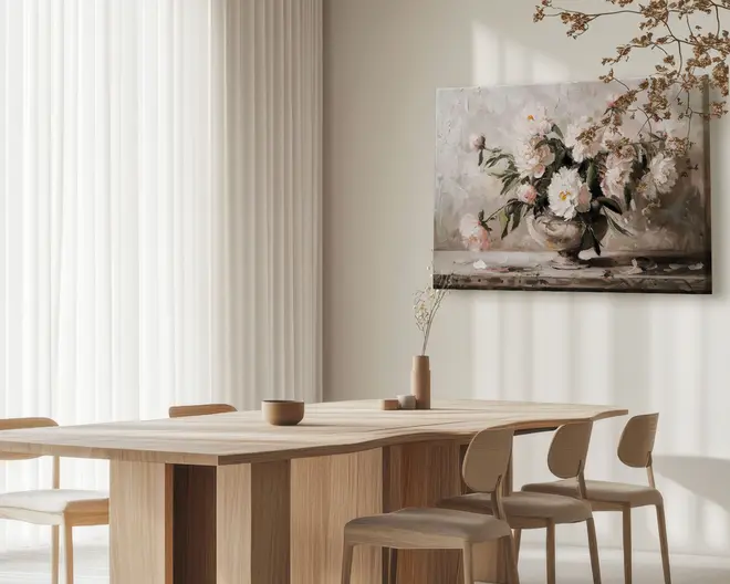 Minimalistisk spisestue med et rektangulært bord i lyst træ og matchende stole. Bordet har rene, lige linjer og en glat overflade. På bordet står en enkel beige vase med en tørret gren samt to små, runde keramikbeholdere. Rummet er blødt oplyst af naturligt lys, der filtreres gennem hvide, gennemsigtige gardiner. På væggen hænger et stort maleri af hvide og lyserøde pæoner i en vase, som tilfører elegance og farve til det neutrale rum. Atmosfæren er rolig, luftig og moderne.