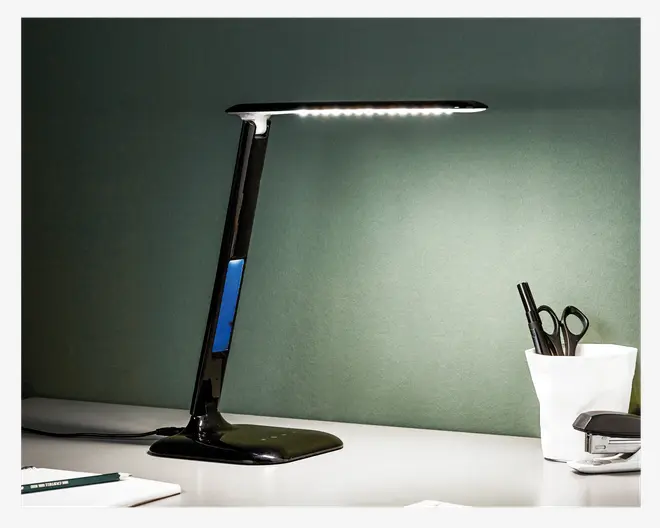 Elegant, moderne skrivebordslampe med blank sort overflade og et slankt, rektangulært LED-lyspanel. Lampen har en skrå arm og en bred, stabil fod. Der er en blå detalje på armen, og lampen er tilsluttet med en synlig ledning. Designet er minimalistisk og passer godt til nutidige arbejdsområder.