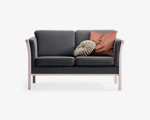 En kompakt to-personers sofa med mørkegråt stofbetræk og bløde sæde- og ryghynder. Sofaen har en ramme og ben i lyst træ, hvilket giver et moderne udtryk. Der medfølger to pyntepuder: én rund og tekstureret i lys beige, og én firkantet i en afdæmpet rustfarve.