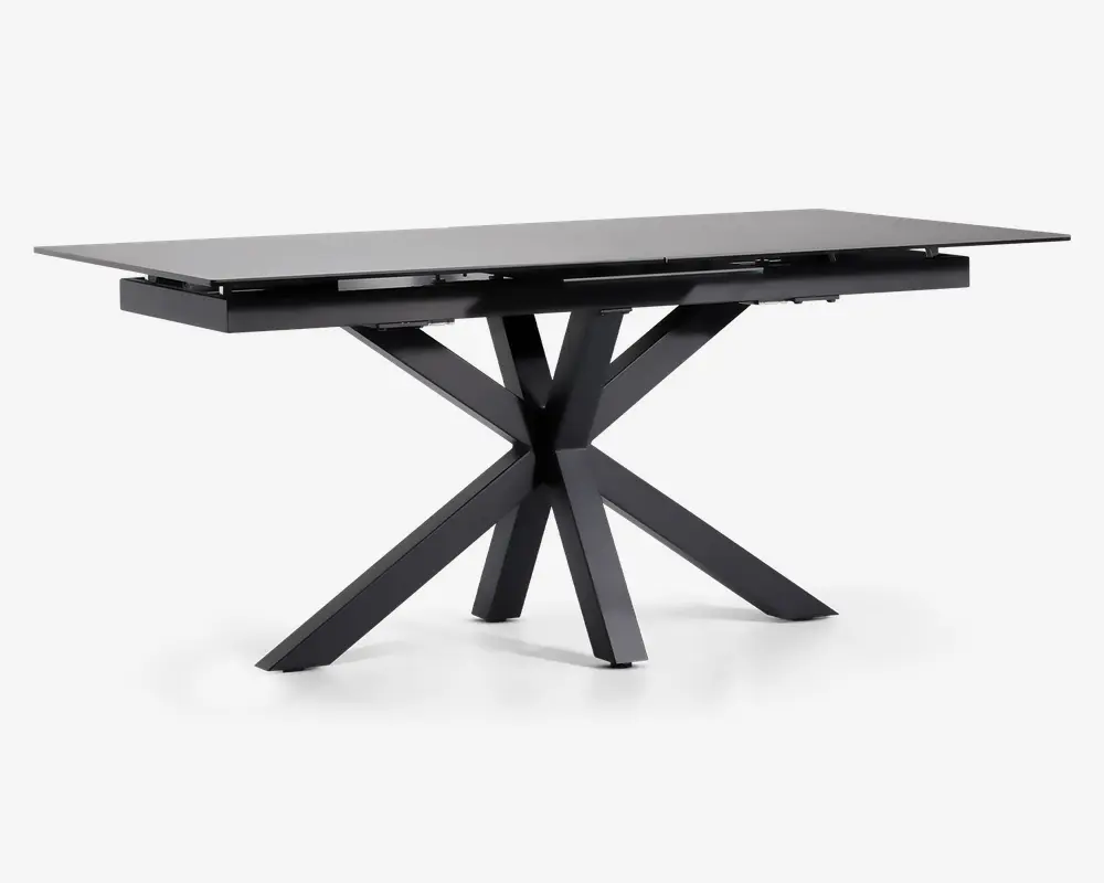 Rektangulært bord med en elegant, mat sort finish. Bordpladen er flad og glat, understøttet af en markant geometrisk base med fire skråtstillede ben, der mødes i midten og giver et moderne, skulpturelt udtryk. Bordet fremstår robust og rummeligt, velegnet til spise- eller arbejdsbrug.