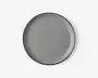 Rund tallerken med en glat, blank lysegrå overflade og en tynd, let hævet kant. Tallerkenens kant er diskret mørkere, hvilket giver et minimalistisk og moderne udtryk. Tallerkenen ser ud til at være lavet af keramik eller porcelæn.