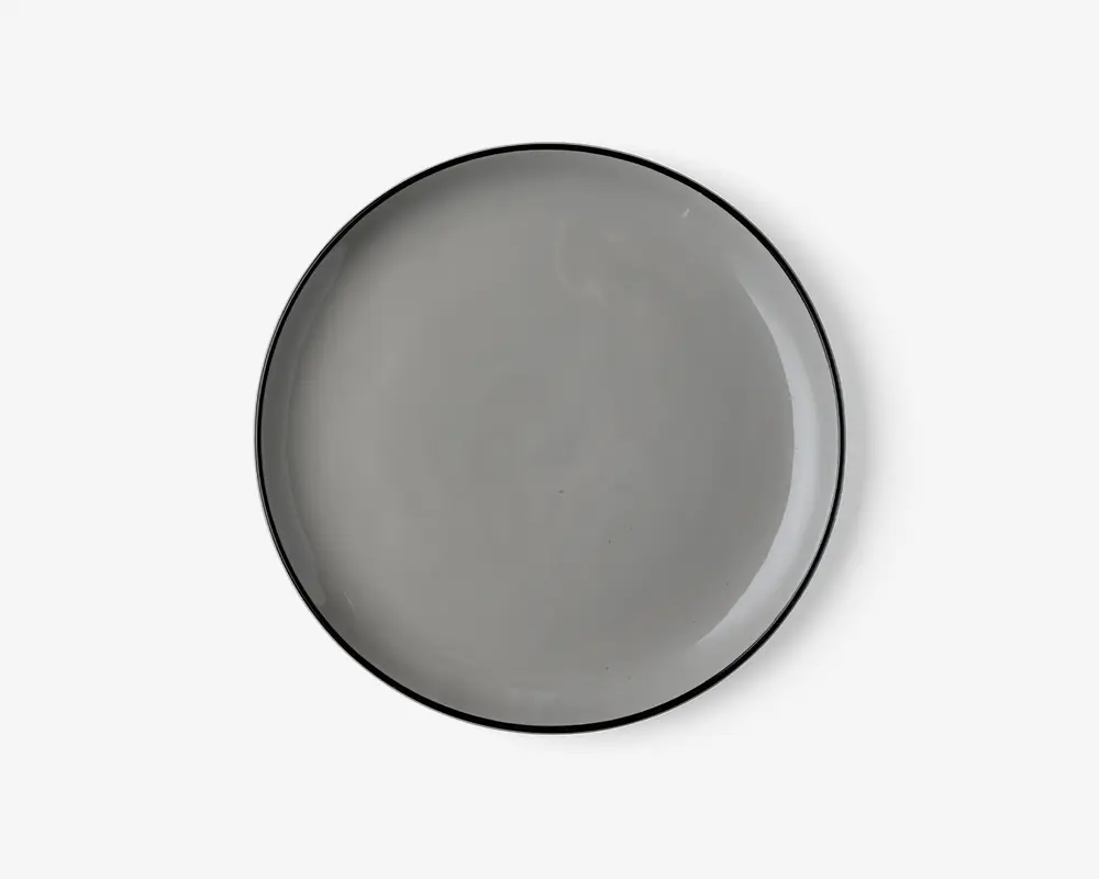Rund tallerken med en glat, blank lysegrå overflade og en tynd, let hævet kant. Tallerkenens kant er diskret mørkere, hvilket giver et minimalistisk og moderne udtryk. Tallerkenen ser ud til at være lavet af keramik eller porcelæn.