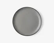 Rund tallerken med en glat, blank lysegrå overflade og en tynd, let hævet kant. Tallerkenens kant er diskret mørkere, hvilket giver et minimalistisk og moderne udtryk. Tallerkenen ser ud til at være lavet af keramik eller porcelæn.