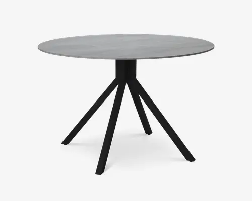 Rundt bord med en glat, lysegrå bordplade og et moderne design. Bordet står på fire skrå, sorte metalben, der mødes i midten og giver stabilitet samt et moderne udtryk. Bordpladens kanter er let affasede for et elegant finish.
