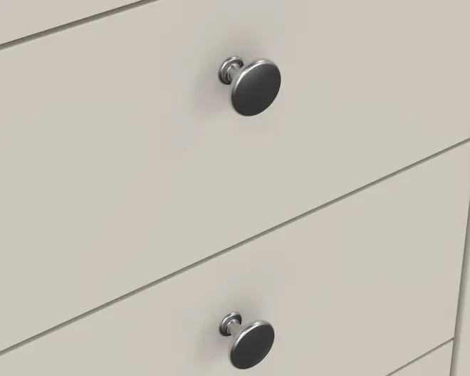 Nærbillede af to skuffer med glatte, matte lyse beige overflader. Hver skuffe har en rund, metalgreb med børstet finish og en let hævet base, hvilket giver et moderne og minimalistisk udtryk. Skuffefronterne er flade med rene linjer og uden synlige samlinger eller dekorative detaljer.