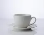 En hvid keramikkop med tilhørende underkop, begge med lodrette riller i overfladen. Koppen har et rundt håndtag og en glat, blank finish, hvilket giver et moderne og elegant udtryk.