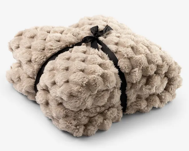 Blød beige faux-fur plaid foldet i en kompakt bunke og bundet med et sort satinbånd.