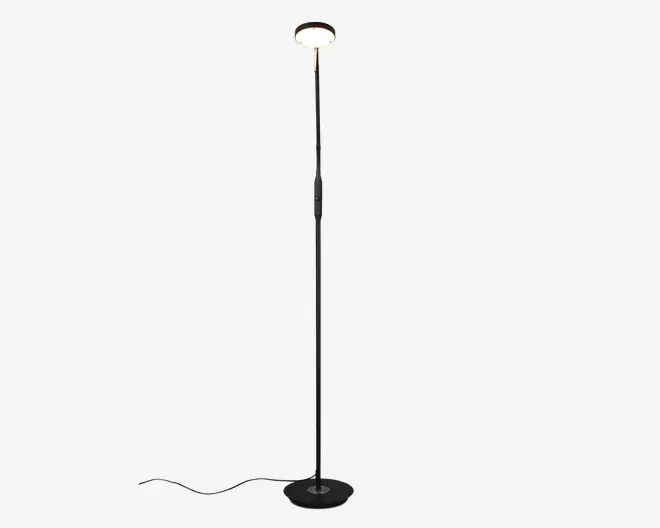 Høj, slank standerlampe med en rund, flad fod for stabilitet. Lampen har et cirkelformet, opadrettet lys øverst, som udsender et blødt, diffust skær. Kroppen er en elegant sort metalstang med et minimalistisk design, og ledningen går ud fra bunden. Der sidder et lille kontrolpanel eller en kontakt et stykke oppe på stangen for nem betjening.