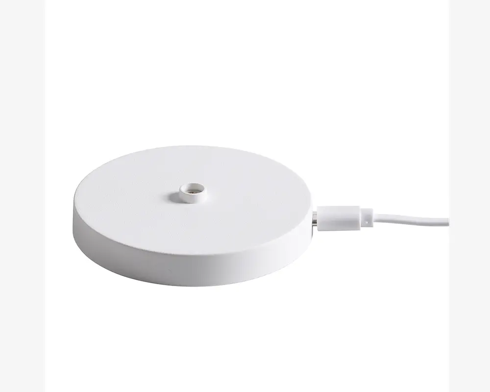 En rund, flad, hvid base med en glat overflade og et lille gevindhul i midten, beregnet til montering af en anden komponent. Basen har et USB-C kabel tilsluttet på siden til strøm eller dataoverførsel.