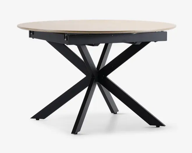Et rundt bord med en lys træbordplade og en moderne, sort metalbase med fire skråtstillede ben, der krydser hinanden i midten og danner en stabil og stilfuld understøtning. Bordpladen har en glat overflade og let skrå kanter.