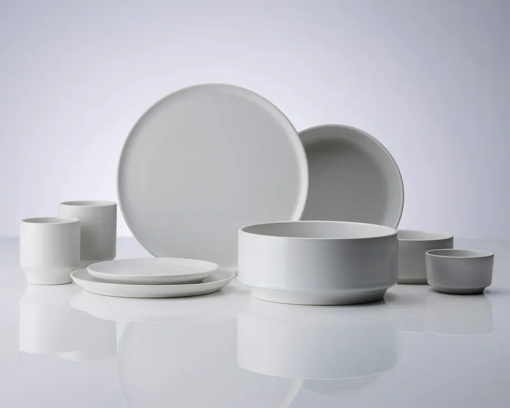 Et sæt minimalistisk, mat hvidt keramikstel bestående af to store middagstallerkener, to mindre sidetallerkener, to cylindriske krus, en stor serveringsskål og to små skåle. Delene har rene, moderne linjer med glatte overflader og ingen dekorative mønstre, hvilket giver et tidløst og alsidigt udtryk, der passer til mange forskellige borddækninger.