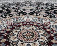 Nærbillede af et tæppe med et indviklet blomstermønster og medaljon-design. Mønsteret består af detaljerede motiver i bordeaux, creme, sort, grå og beige nuancer. Teksturen ser blød og tæt ud, hvilket fremhæver de dekorative detaljer og farvekontraster.