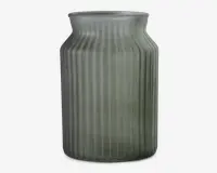 Høj cylindrisk beholder lavet af mat glas med et svagt grønligt skær. Overfladen har lodrette rillede linjer, der giver tekstur, og halsen er let udvidet med en glat kant. Designet er minimalistisk og moderne.