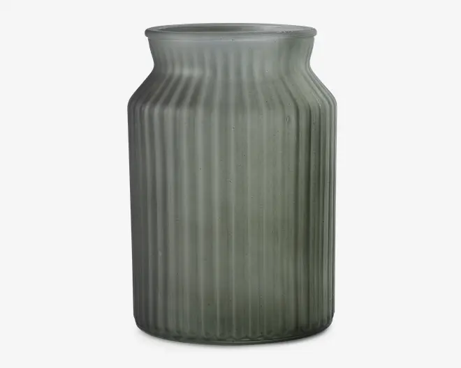 Høj cylindrisk beholder lavet af mat glas med et svagt grønligt skær. Overfladen har lodrette rillede linjer, der giver tekstur, og halsen er let udvidet med en glat kant. Designet er minimalistisk og moderne.