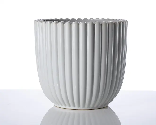 En hvid keramisk beholder med lodrette riller og bølget kant. Overfladen er blank, og formen er cylindrisk med en let afrundet bund. Designet er moderne og minimalistisk, velegnet til dekorative formål.