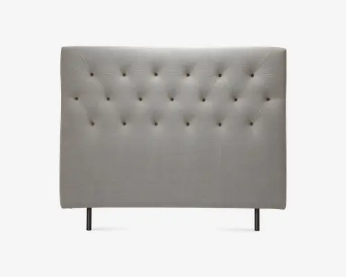 Polstret sengegavl i lysebeige stof med rektangulær form. Har et knapstukket design med jævnt fordelte knapper, der danner et diamantmønster på overfladen. Sengegavlen har en glat, polstret finish for ekstra komfort og understøttes af to solide metalben i bunden.