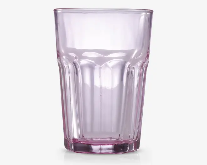 Højt, transparent drikkeglas med en diskret lyserød tone. Glasset har et facetteret design med lodrette riller langs siderne, hvilket giver et godt greb og et stilfuldt udseende. Randen er glat og let udadbuet, og bunden er tyk og solid for ekstra stabilitet.